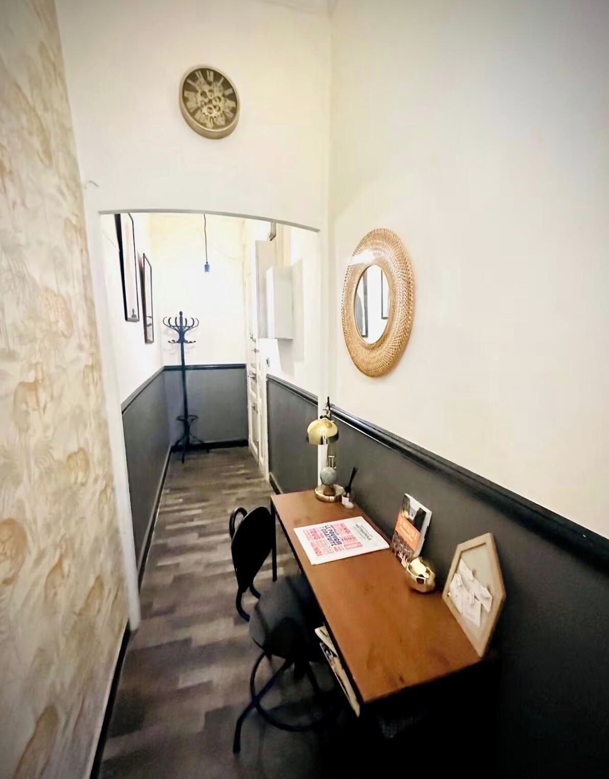 A narrow hallway with a wooden desk, a chair, a lamp, and a mirror on the wall.