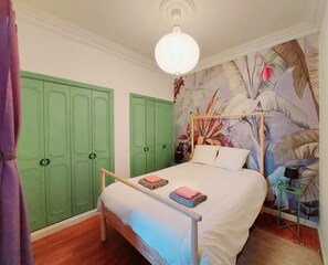 A bedroom with a bed, green wardrobes, a floral mural, and a hanging light fixture. - Appart "L'échappée Belle" Montpellier center, Train station (Montpellier)
