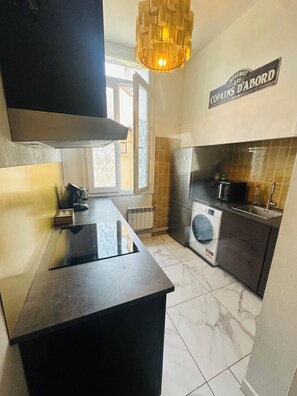 A modern kitchen with a central island, a built-in washing machine, and a hanging light fixture. - Appart "L'échappée Belle" Montpellier center, Train station (Montpellier)
