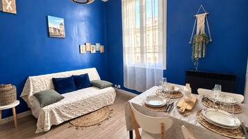 A room with a blue wall, a white sofa, a dining table set with plates and glasses, and a hanging macrame plant.