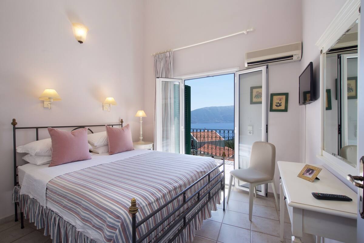 Ein Schlafzimmer mit Bett, Schreibtisch und Stuhl. Ein Fenster bietet Blick auf Gebäude, und es gibt einen Balkon.