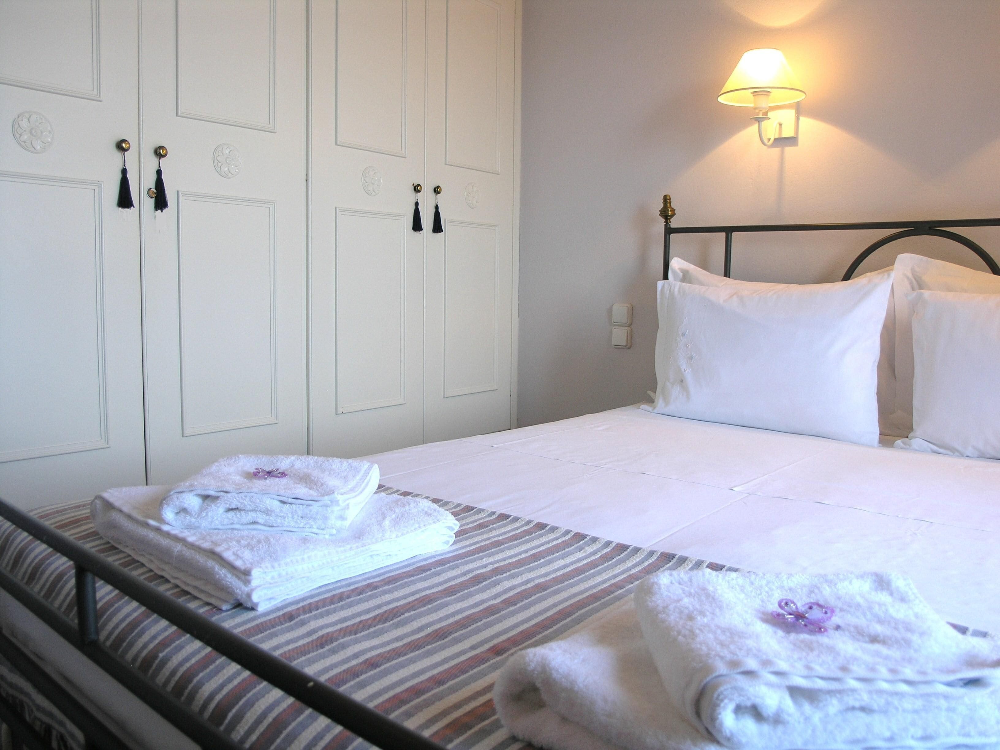 Un lit bien fait, avec des draps blancs, une couvre-lit à rayures et deux serviettes ornées de motifs floraux sur le côté.