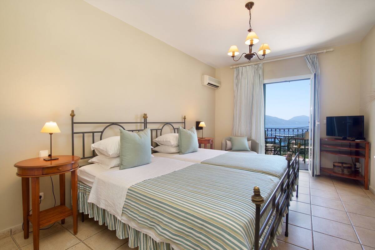 Ein Hotelzimmer mit zwei Betten, einem Fernseher, einem Balkon mit Blick und einem Kronleuchter.