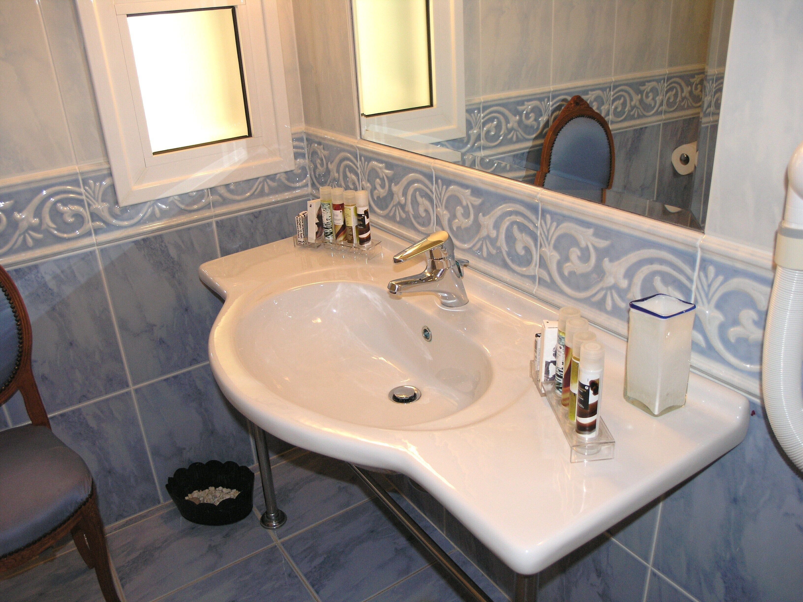 A bathroom with a white sink, two faucets, a mirror, and a towel dispenser.