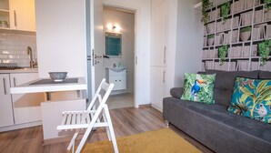Un salon moderne avec un canapé gris, des coussins colorés, un fauteuil blanc et une bibliothèque remplie de livres et de plantes.