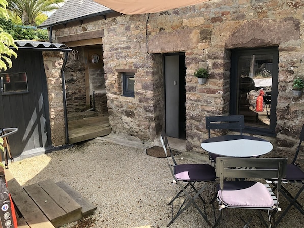 A rustic stone building with a wooden door, a small window, and a table with chairs.