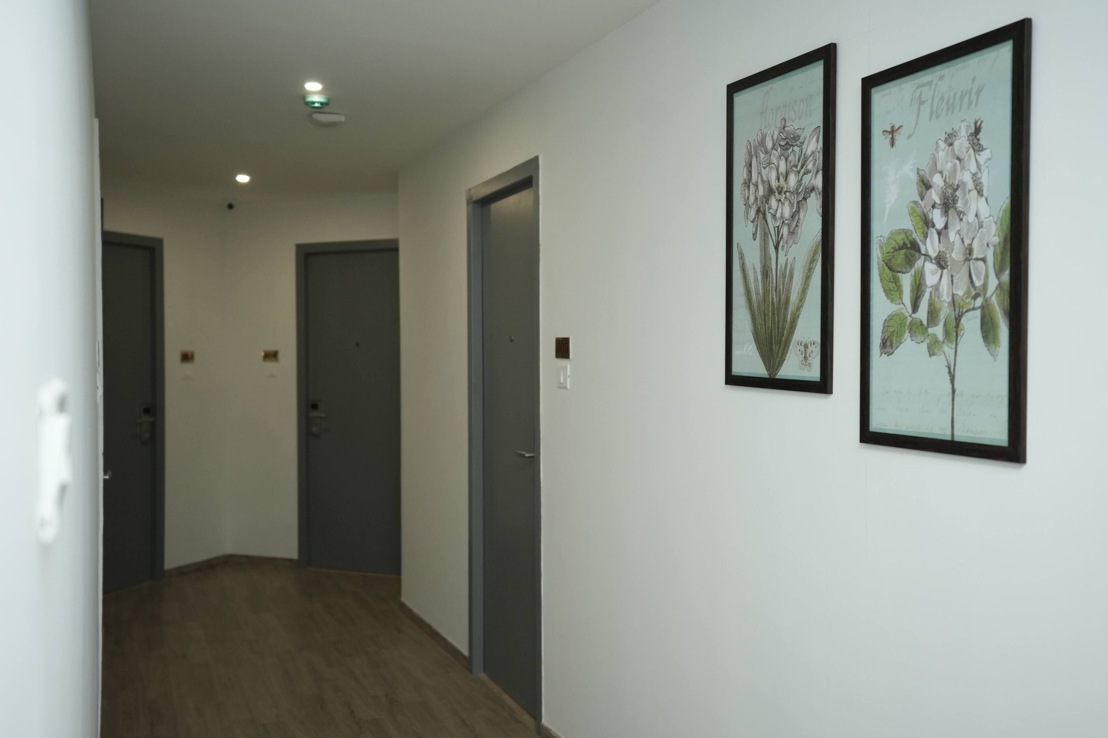 A hallway with wooden flooring, white walls, and two framed botanical prints.