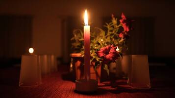 A candlelit table with a lit candle in the center, surrounded by candles in glass holders, and a vase with red flowers.