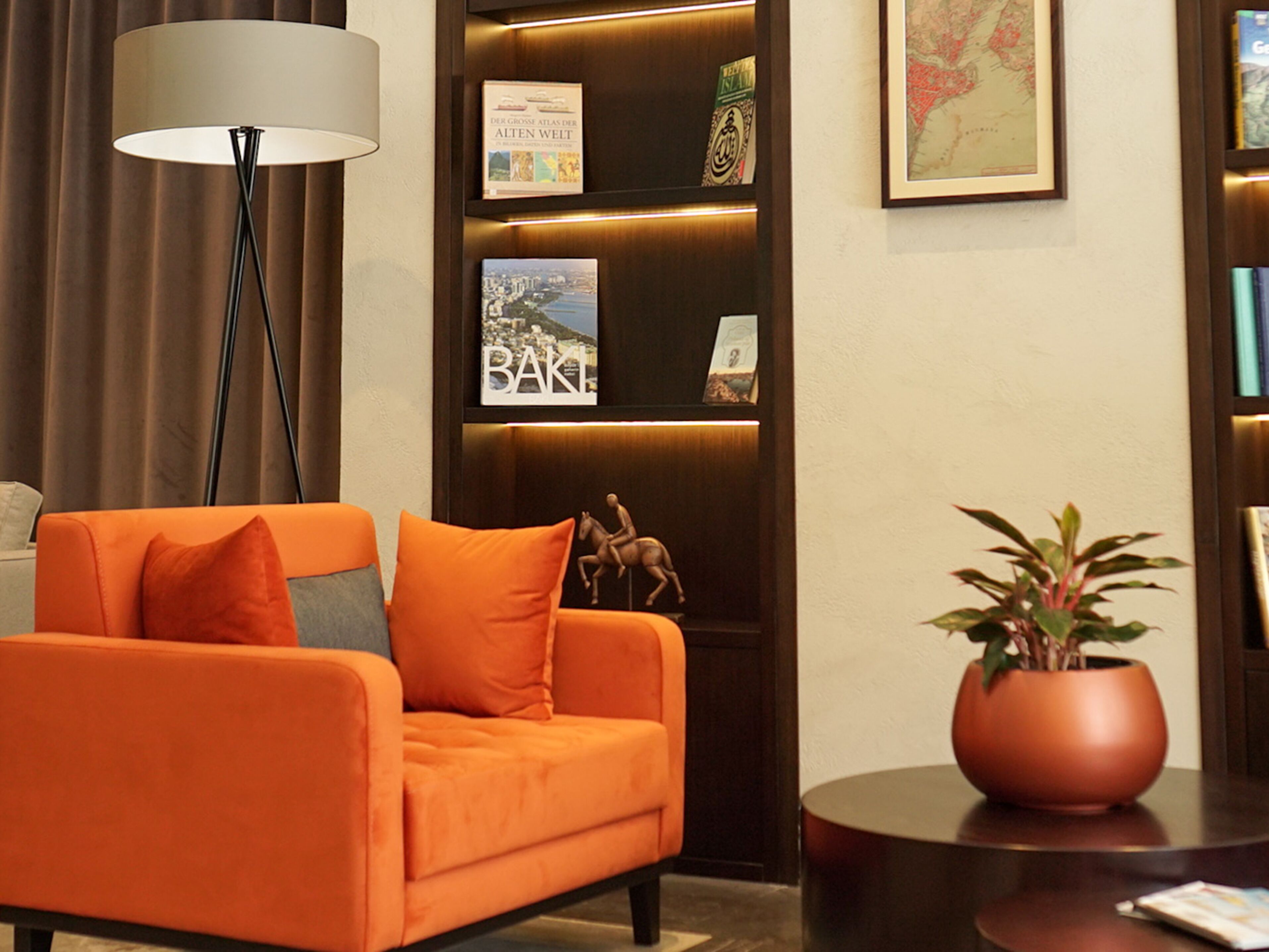 A modern living room with an orange sofa, a floor lamp, a bookshelf with books and decorative items, and a potted plant on a side table.