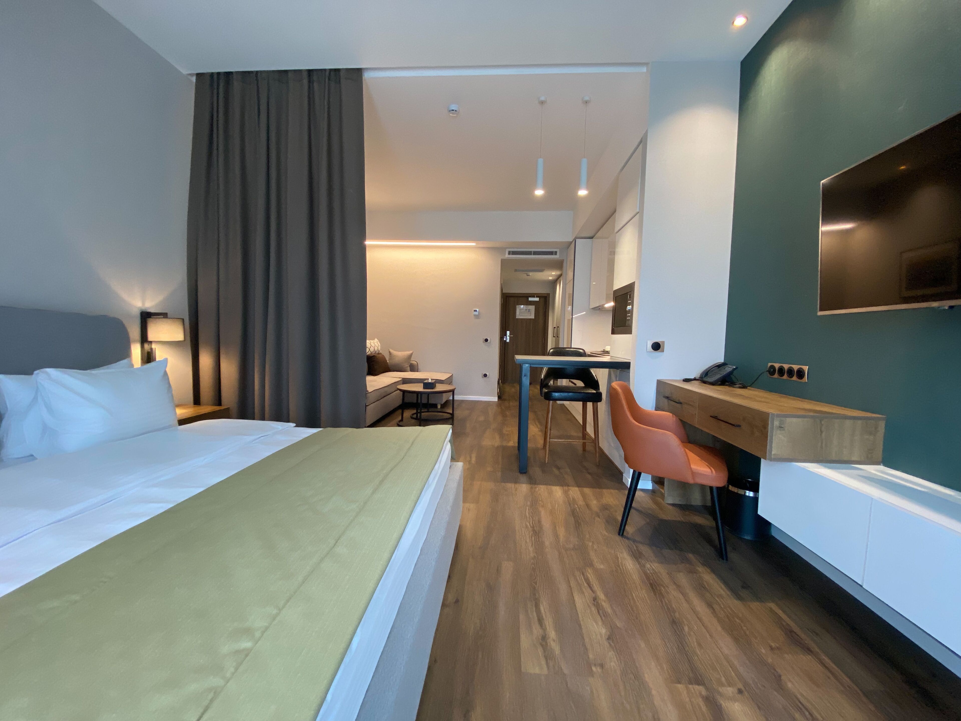 Ein Hotelzimmer mit Bett, Schreibtisch mit Stuhl, einer kleinen Couch und einem an der Wand befestigten Fernseher.