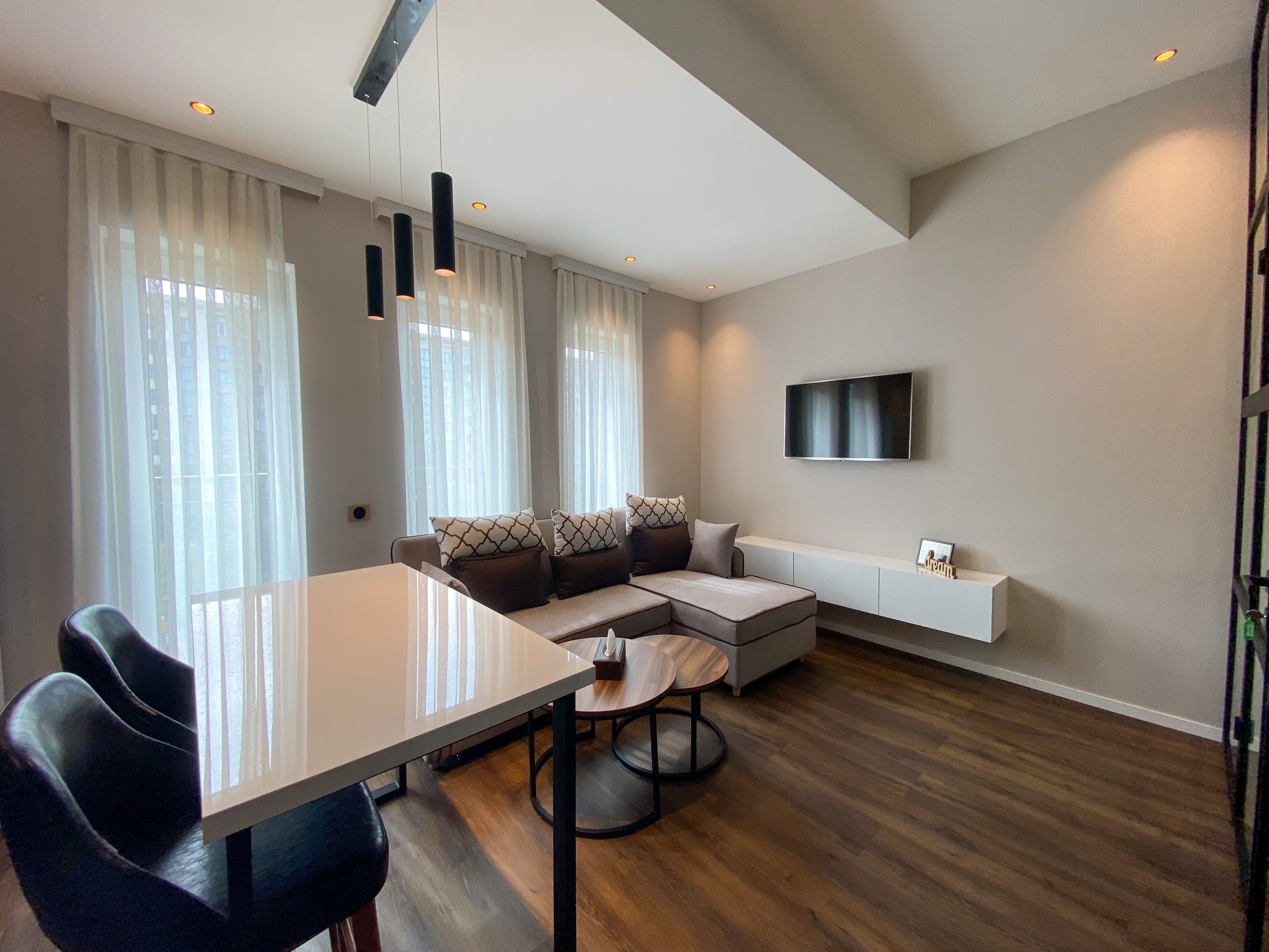 A modern living room with a dining table, sofa, and TV mounted on the wall.