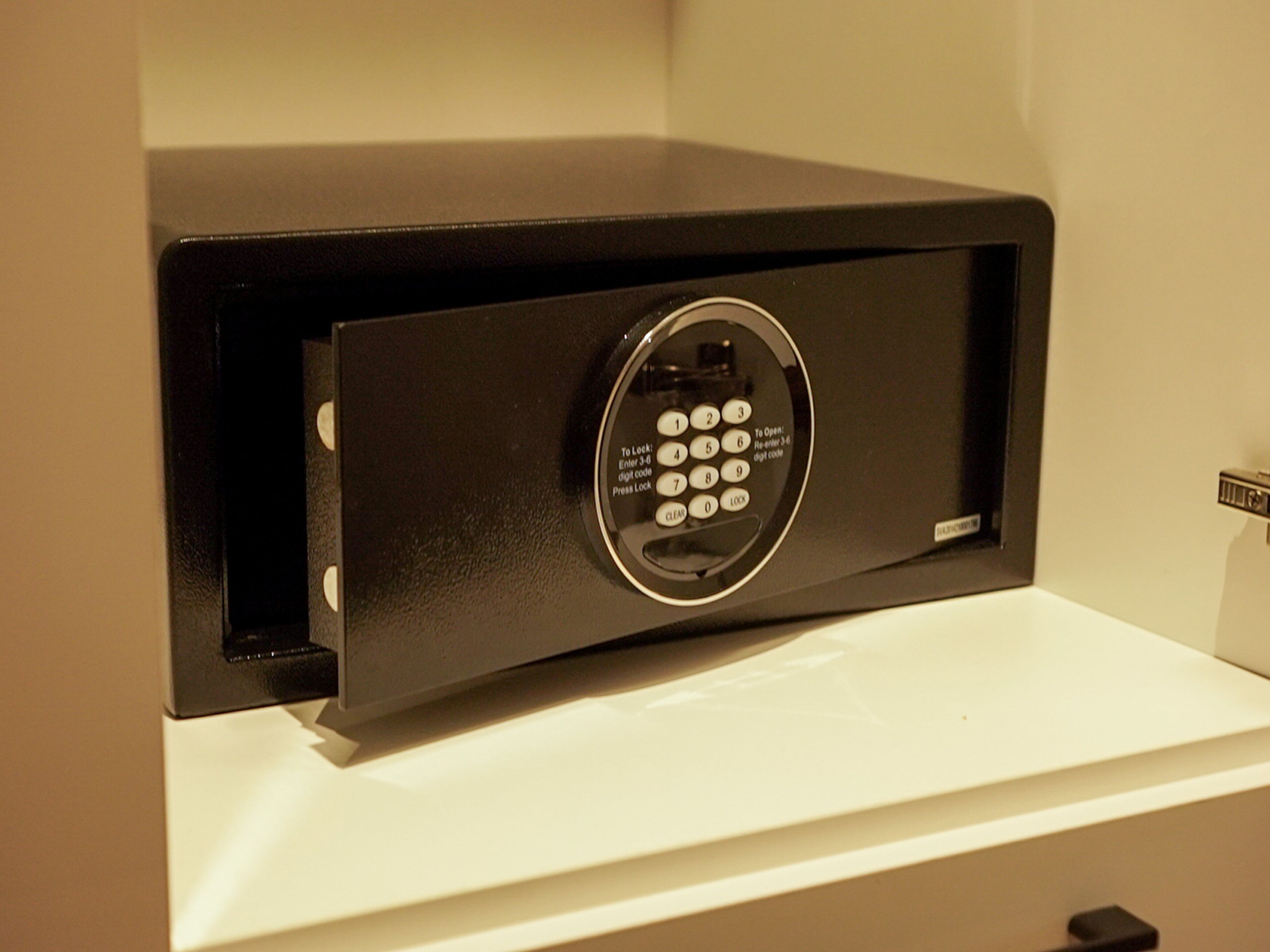 A black safe with a keypad on a white shelf.