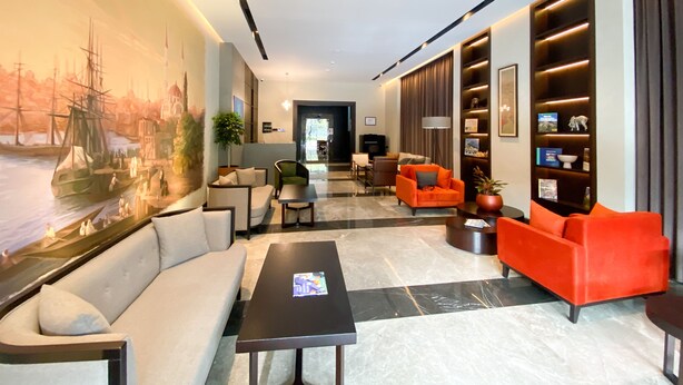 Una moderna hall d'albergo con un grande murale, posti a sedere confortevoli, una reception e un'illuminazione curata.