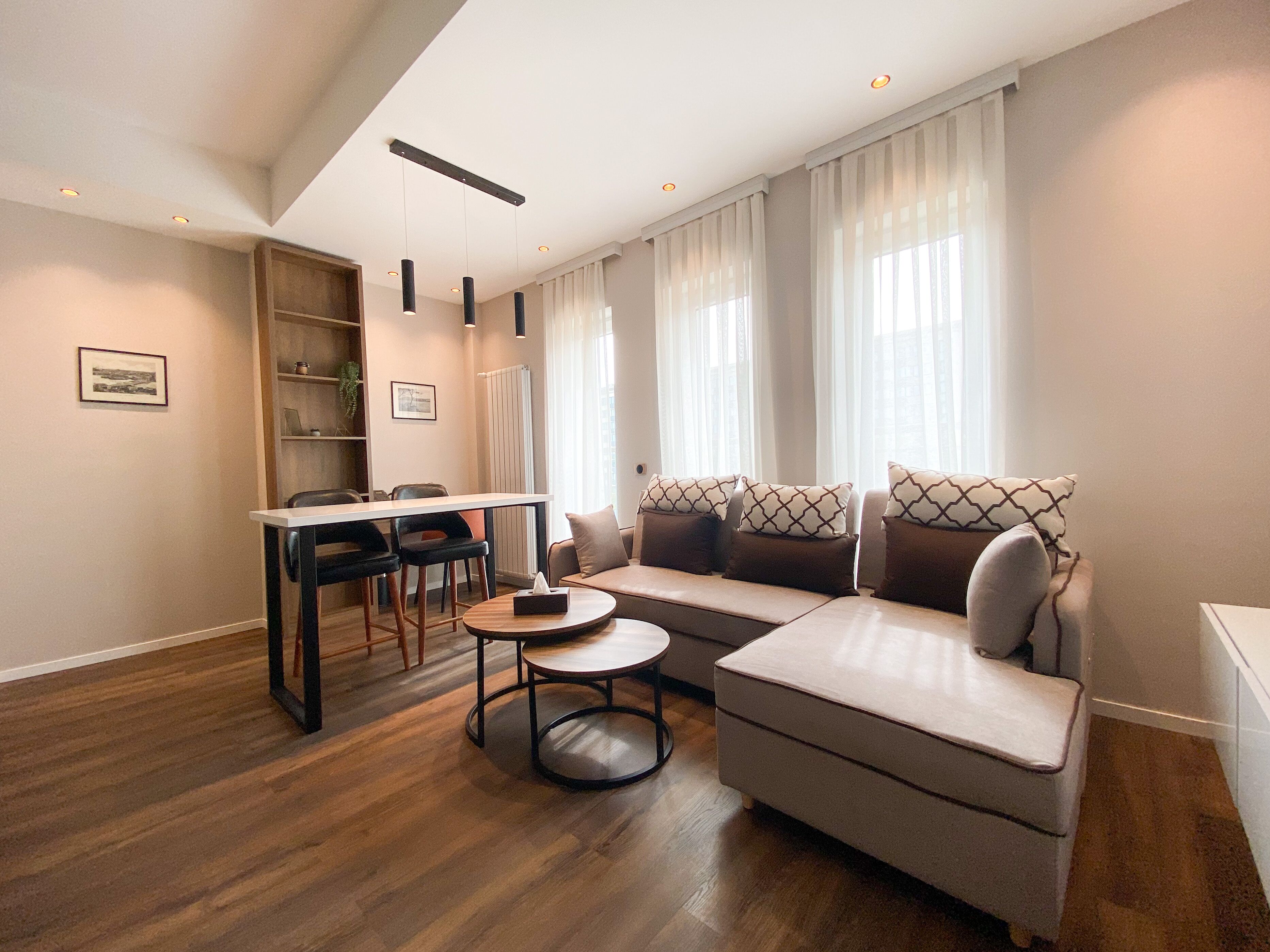 A modern living room with a sofa, a dining table, and chairs. There is a small round table in the center.