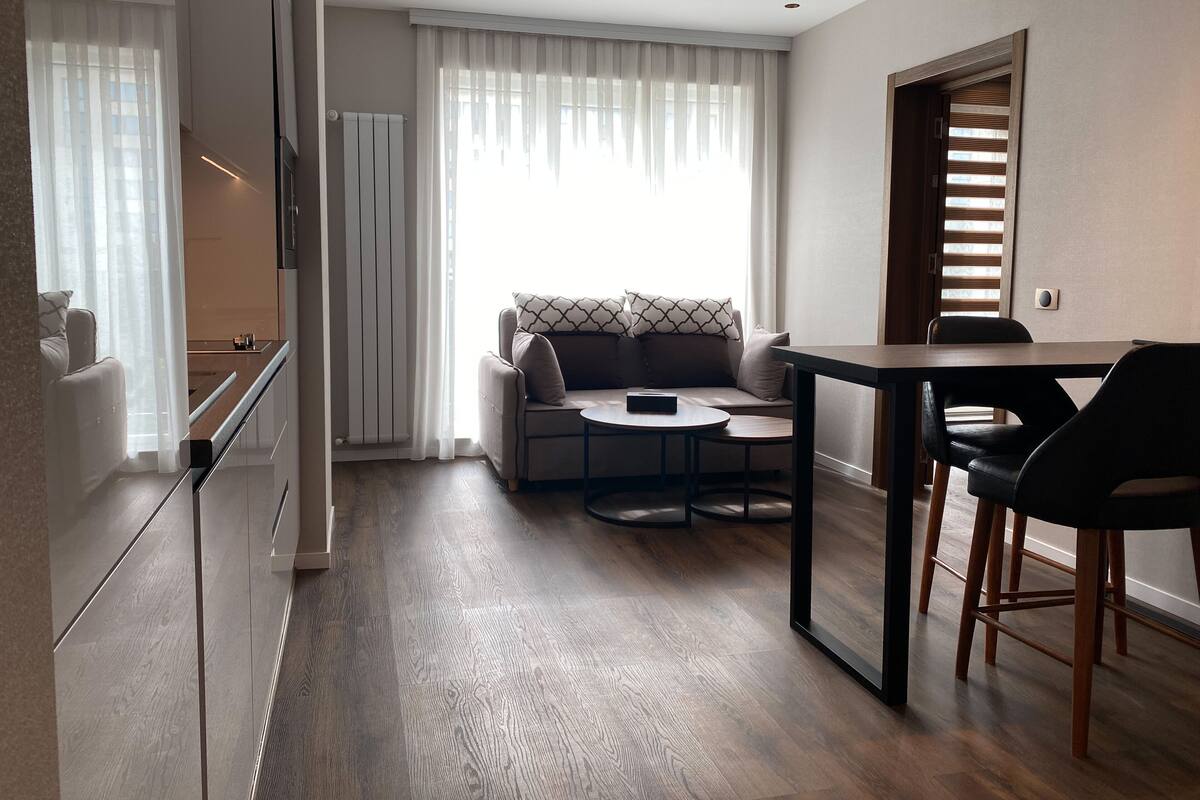 A modern living room with a sofa, a small round table, and a dining table with chairs.