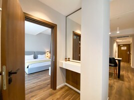 Een hotelkamer met een houten vloer, een bed met witte lakens, een nachtkastje met een lamp en een grote spiegel.