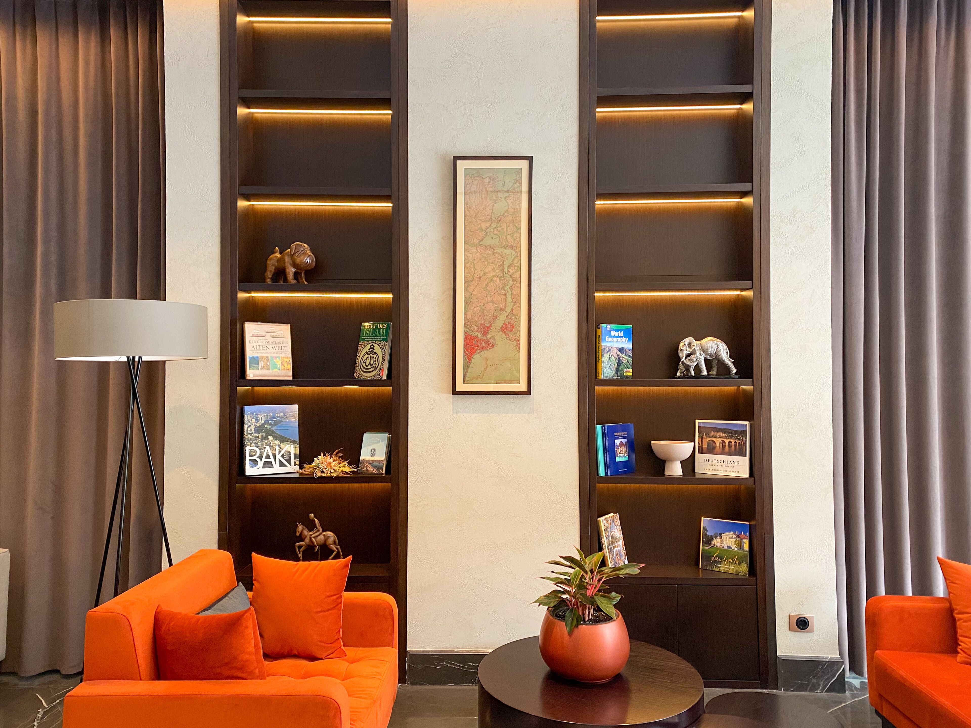 A modern living room with orange sofas, a floor lamp, and a bookshelf with books and decorative items.