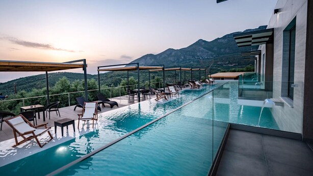 A modern infinity pool with lounge chairs and tables, overlooking a mountainous landscape. - Serenity Suites Sea View 4 (Zacharo)