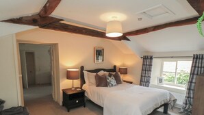 Une chambre à coucher avec un lit, deux tables de chevet avec des lampes, une fenêtre avec des rideaux et une porte donnant sur une autre pièce.