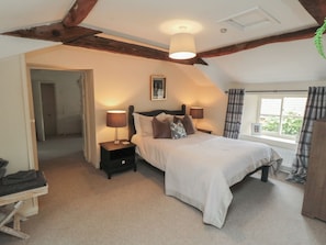 A bedroom with a bed, two bedside tables with lamps, a window with curtains, and a door leading to another room.
