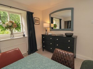 A room with a window, a dresser, a mirror, a table, and a chair. - Black Horse Cottage (Northallerton)