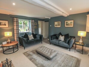 A living room with two dark sofas, a grey ottoman, and two small tables with lamps.