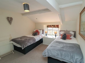 Une chambre avec deux lits, une fenêtre avec des rideaux, un luminaire fixé au mur et un radiateur.