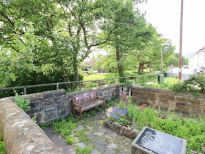 Un banc en pierre orné d’une plaque, entouré d’un mur de pierre et d’une végétation luxuriante.