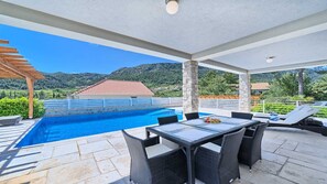 Uma área externa coberta com piscina, mesa de jantar e cadeiras.