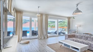 A spacious living room with a large window, a sofa, a TV, and a ceiling fan. - Villa Luxoria - for 10 guests with 4 bedrooms, a private pool and a spa by MyWaycation (Jelsa)
