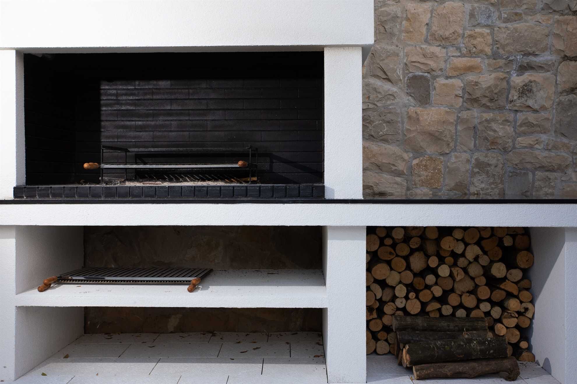 Una chimenea moderna al aire libre con un fondo de pared de piedra, una rejilla para leña y un montón de leña.