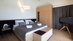 A modern bedroom with a bed, bedside tables, a wardrobe, a TV, and a built-in bench.