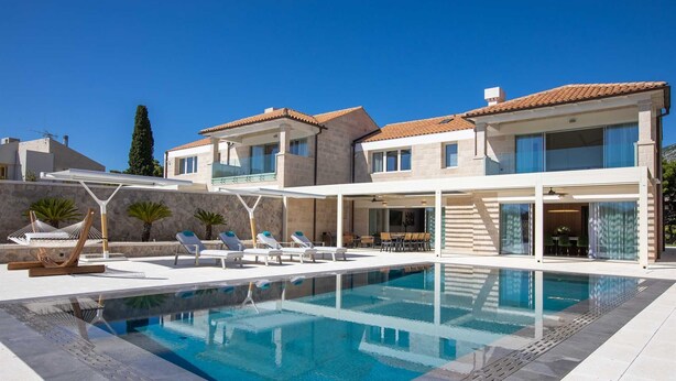 A modern villa with a swimming pool, outdoor seating, and a stone wall.