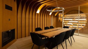 A modern dining area with a wooden table and black chairs, a wine rack with bottles, and a unique curved ceiling design.