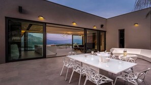 A modern outdoor dining area with a table and chairs, a champagne bucket, and a view of the mountains. - Villa Masterpiece - high end luxury vill with 5 bedrooms on island Korčula by MyWaycation (Grad Korcula)