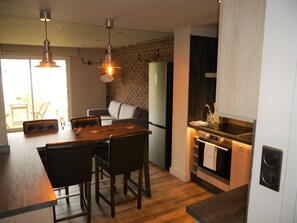 A modern kitchen with a dining area, wooden flooring, and a brick wall.