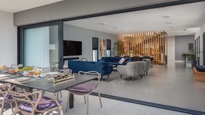 A modern living room with a dining area, featuring a large TV, sofas, and a decorative wooden partition. - Villa Endless Summer - 5 Star beachfront villa with a pool by MyWaycation (Vinišće)