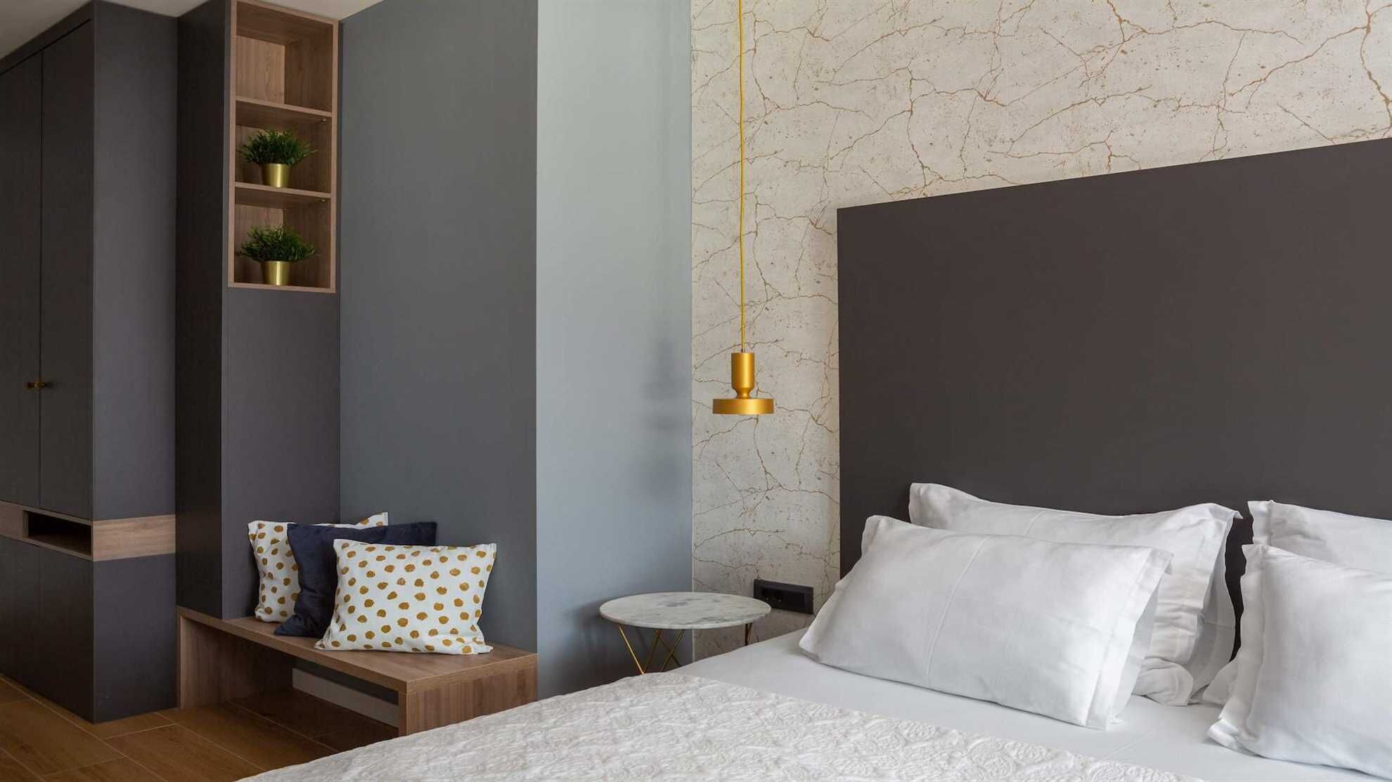 A modern bedroom with a large bed, a bedside table, a small round table, and a built-in shelving unit with plants.
