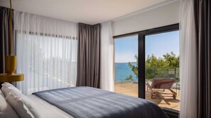 Une chambre avec un grand lit, une vue sur la mer et un balcon équipé d’une chaise.