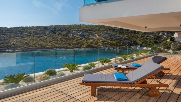 A wooden deck with two lounge chairs and a table, overlooking a clear blue pool and a mountainous landscape. - Villa Endless Summer - 5 Star beachfront villa with a pool by MyWaycation (Vinišće)