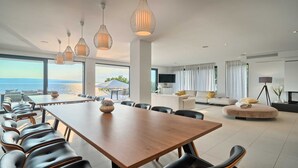 A modern living room with a large wooden table and chairs, a sofa, and a TV. There is a view of the sea through large windows. - Villa Platinum - outstanding beachfront villa with 9 bedrooms by MyWaycation (Brela)
