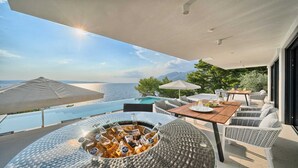 A modern outdoor dining area with a pool, overlooking the sea, and a bar with bottles. - Villa Platinum - outstanding beachfront villa with 9 bedrooms by MyWaycation (Brela)