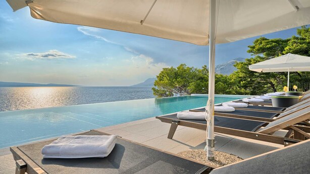 An infinity pool with lounge chairs and umbrellas, overlooking a body of water and greenery. - Villa Platinum - outstanding beachfront villa with 9 bedrooms by MyWaycation (Brela)
