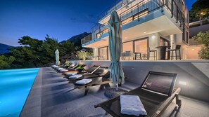 Un espace piscine aménagé sur le toit, avec des chaises longues, des parasols et une vue sur la montagne.