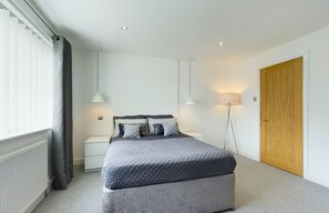 A modern bedroom with a large bed, bedside tables, a wooden door, and a radiator. - Inviting 2-bed House in Newcastle Upon Tyne (Newcastle-upon-Tyne)