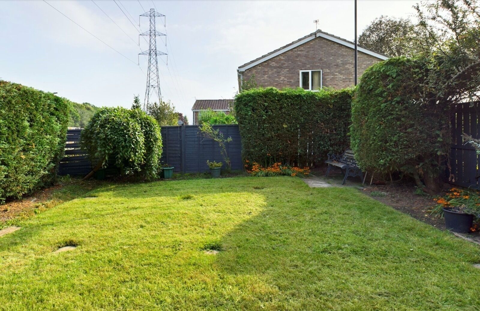 A well-maintained backyard with a lawn, a wooden fence, and a house in the background.