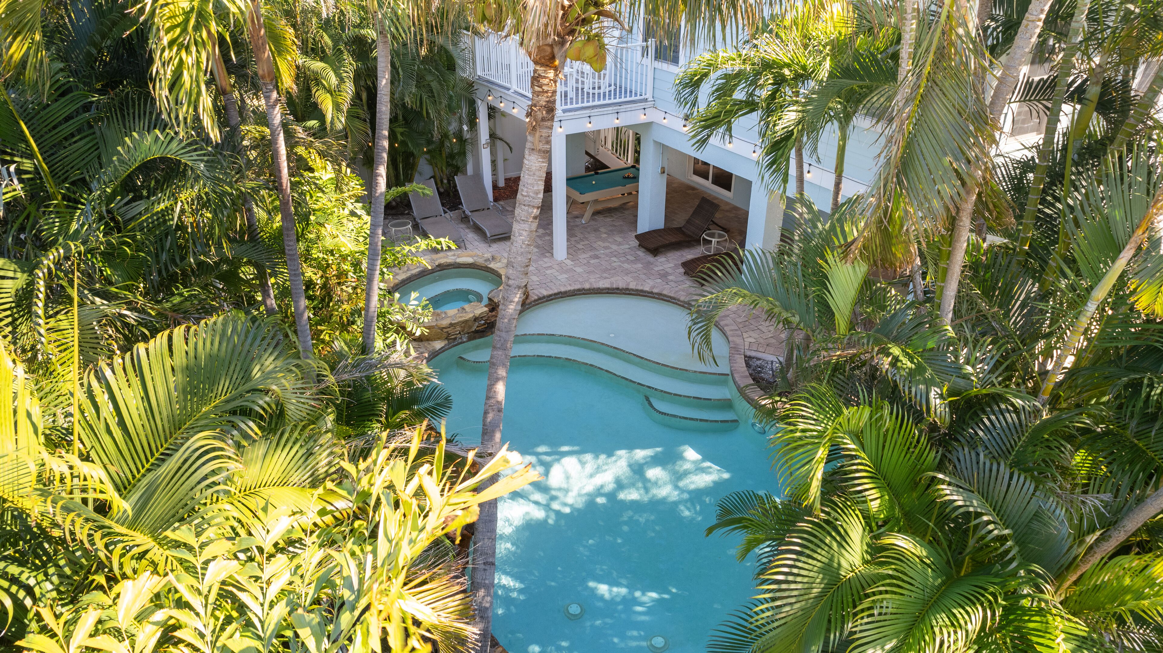 A pool surrounded by lush greenery and a white building with a balcony.