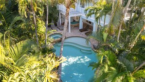 Ein Pool, umgeben von üppigem Grün und einem weißen Gebäude mit Balkon.