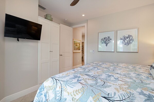 A bedroom with a bed, a TV mounted on the wall, and two framed pictures on the wall.