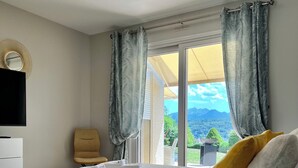 Une chambre avec un lit, une chaise, une télévision et une vue sur l’extérieur.